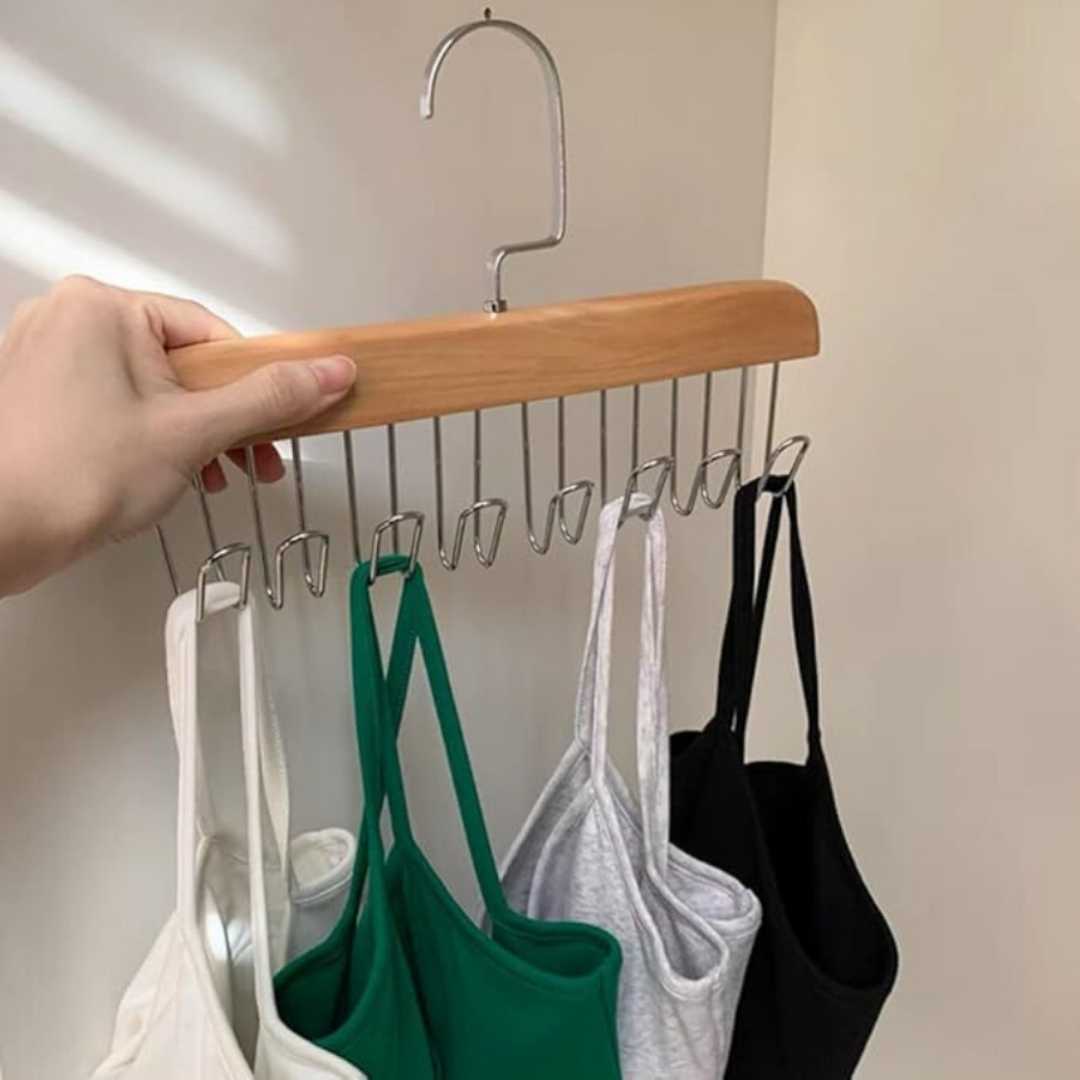 Hand holding a wooden hanger with multiple small hooks displaying various tank tops.