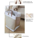 Beige and white laundry basket with brown leather handles on a carpeted floor.