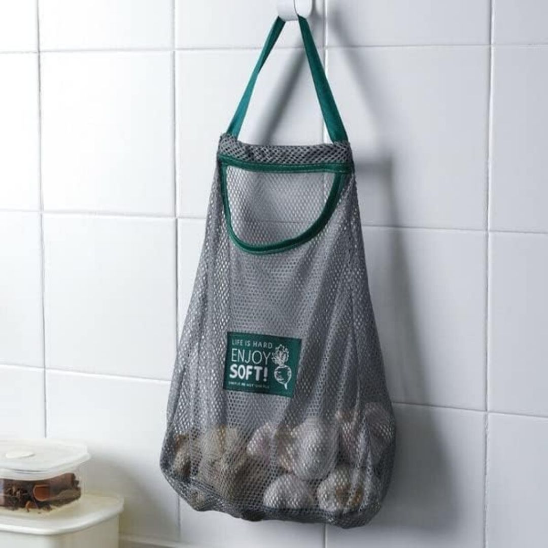 Mesh bag with green trim hanging on a tiled wall, containing items.