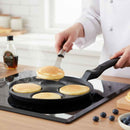Person cooking pancakes on a non-stick pan with a spatula, surrounded by kitchen items.