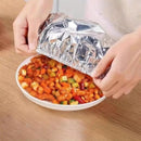 Person opening a foil-wrapped dish of colorful vegetables on a wooden table