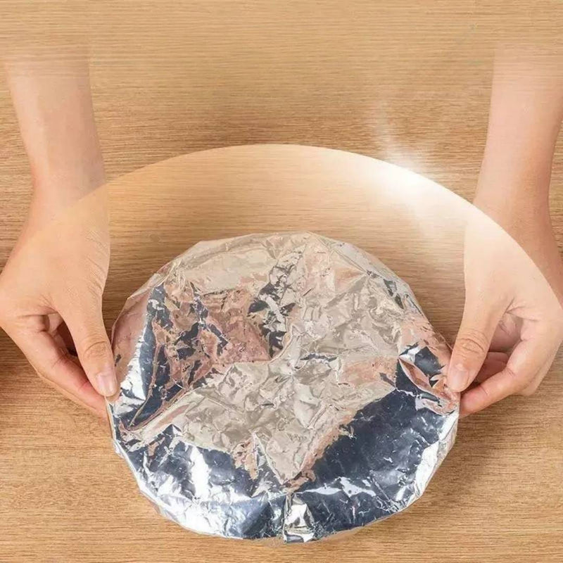 Person holding a round object wrapped in foil on a wooden surface