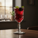 Red cocktail with ice and a mint leaf in a decorative glass on a wooden table.