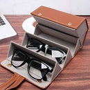 Black sunglasses in an open brown and beige eyewear case on a wooden surface with a laptop in the background.