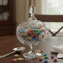 Clear glass candy dish with colorful candies on a wooden table.