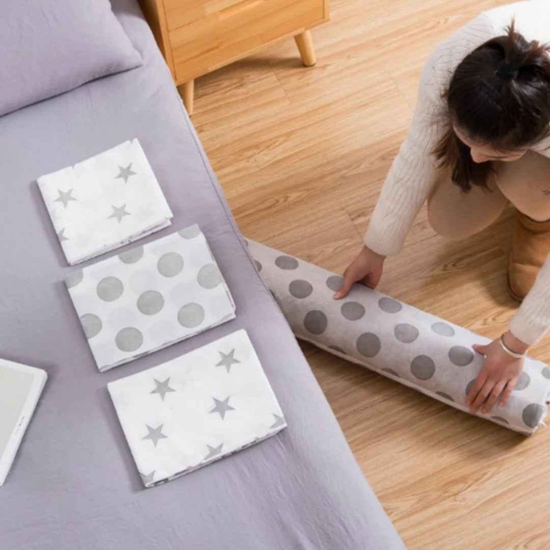 Person rolling out a polka dot mat on a wooden floor next to a bed.
