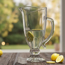 Clear glass pitcher with lemon slices on a wooden surface outdoors