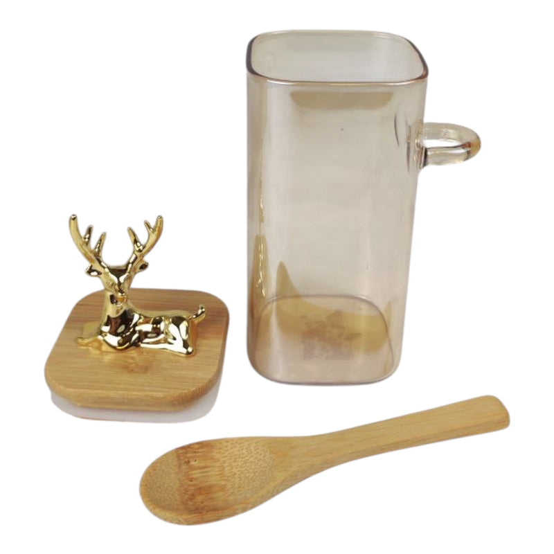 Clear glass mug with gold handle, wooden spoon, and decorative deer figure on a white background