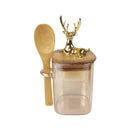 Glass jar with bamboo lid and spoon, featuring a deer design on the lid, on a white background.