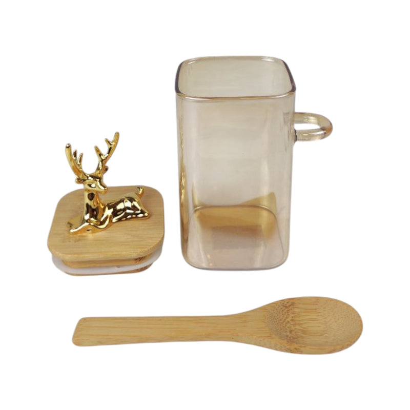 Glass mug with gold deer figure, wooden coaster, and wooden spoon on a white background