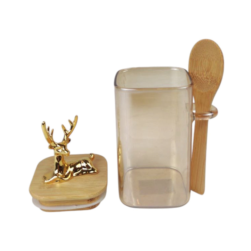 Decorative container with gold deer figure, glass mug, and wooden spoon on a white background