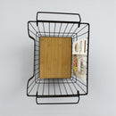 Wall-mounted metal basket with a wooden board and magazines on a light gray background