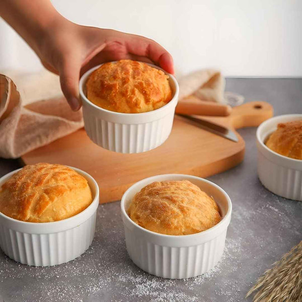 Baked goods in white ramekins on a wooden board with a hand holding one ramekin available at cupindy.com