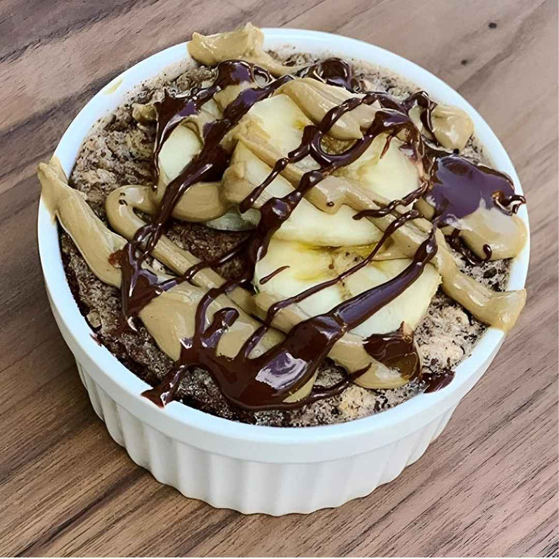 Dessert in a white ramekin with sliced bananas and chocolate drizzle on a wooden surface available at cupindy.com