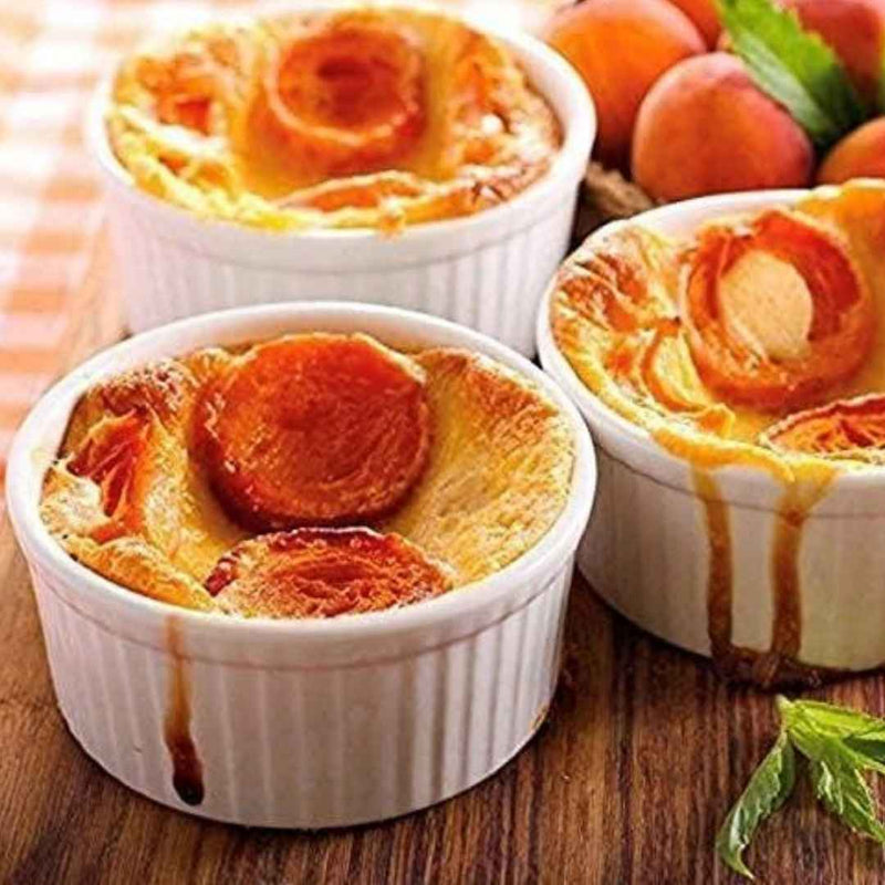 Three small desserts with peach slices on top in white ramekins on a wooden surface available at cupindy.com