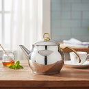 Silver teapot with gold handle on a wooden table with a blurred kitchen background