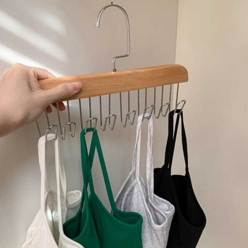 Hand holding a wooden hanger with multiple small hooks displaying various tank tops.