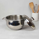 Stainless steel pot with lid on a light gray surface, with wooden utensils in the background.