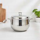 Stainless steel pot on a kitchen counter with a cutting board and plant in the background