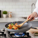 Person cooking vegetables and chicken in a wok on a gas stove with a wooden spatula.