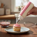 Person using a pink and white icing dispenser to frost a cupcake on a wooden table.
