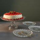Strawberry cake on a glass stand with decorative plates and forks on a dark background