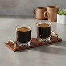 Two glasses of dark liquid on a wooden tray with gold handles, set against a neutral background.