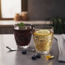 Two glasses of iced tea and a purple drink with a spoon and blueberries on a table.