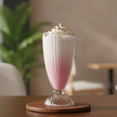 Pink milkshake with whipped cream in a glass on a wooden coaster, blurred indoor background