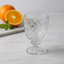 Clear glass goblet with diamond pattern on a white surface with oranges and mint leaves.