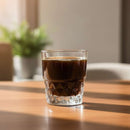 Glass of dark liquid on a wooden table with a blurred background