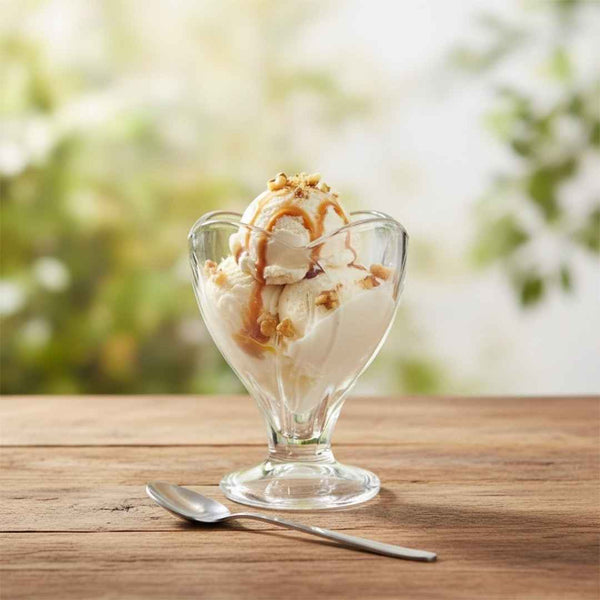Glass dish with ice cream and caramel sauce on a wooden table with a blurred natural background