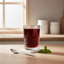 Glass of dark red liquid on a wooden surface with a spoon and mint leaves, blurred background