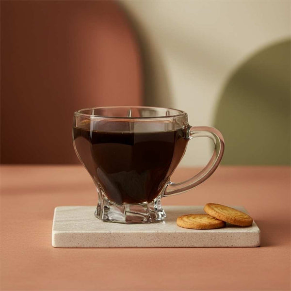 Clear glass mug filled with dark liquid on a coaster with cookies, against a warm-toned background.