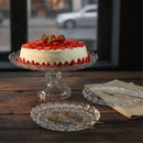 Decorative cake with strawberries on a glass stand on a wooden table.