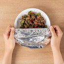 Person wrapping a plate of food in tinfoil on a wooden table