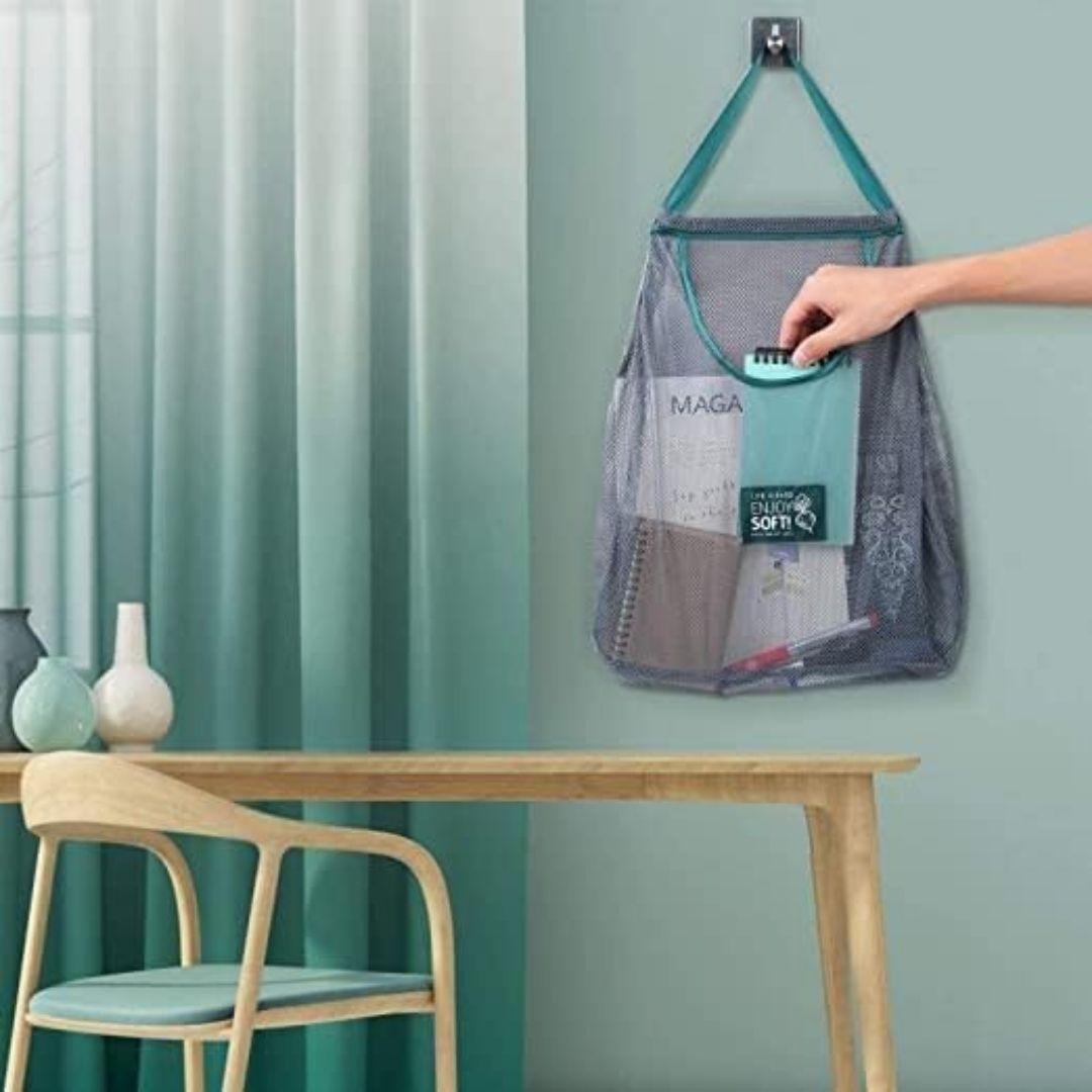 Handy mesh storage bag with a hand reaching in to retrieve items from it, hanging on a hook against a teal wall.