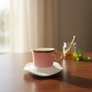 Pink teacup with gold rim and handle on a white saucer on a wooden table.