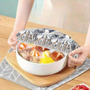Person holding a bowl with food wrapped in aluminum foil on a wooden table.