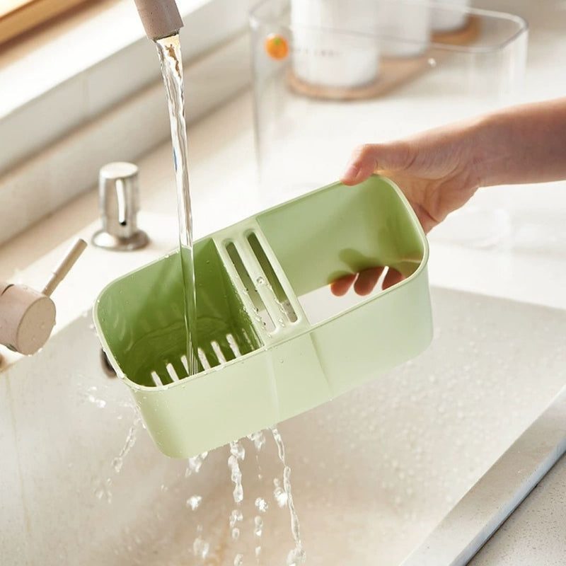 Green kitchen sink caddy being rinsed under running water in a kitchen.