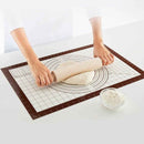 Person rolling dough on a silicone baking mat with a bowl of flour on a white surface