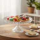 Clear glass cake stand with various pastries on a wooden table.