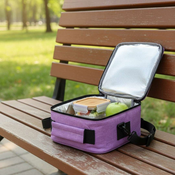 Purple insulated lunch bag with food items on a wooden bench outdoors