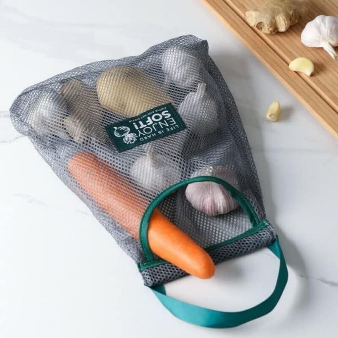 Reusable mesh produce bag with carrots and garlic on a white surface