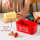 Red butter container with lid as a cutting board, butter being spread on bread.