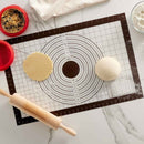 Baking setup with a rolling pin, dough, and a measuring mat on a marble surface.