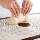 Person kneading dough on a silicone baking mat with grid lines.