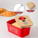 Red butter container with wooden lid and knife, surrounded by croissants on a light gray background.