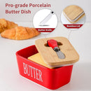 Red butter dish with wooden lid and knife, surrounded by croissants on a light background.