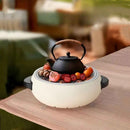 Black teapot on a small stove with fruits on a wooden table